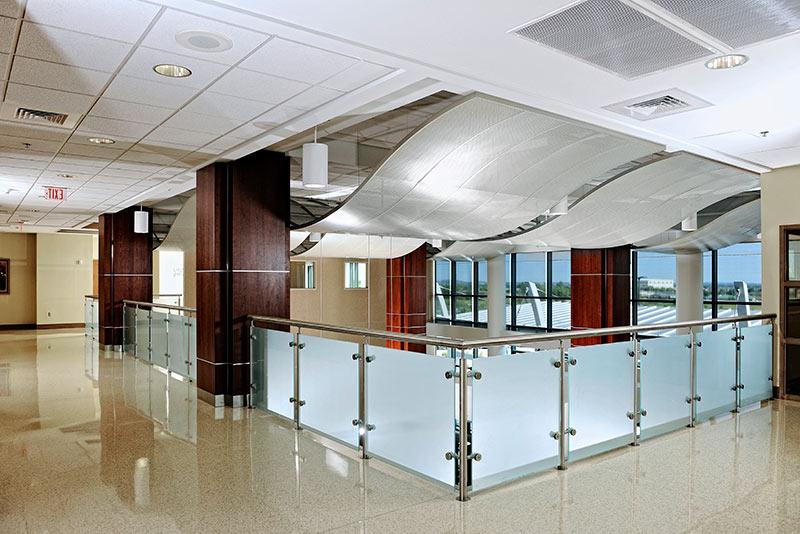 Interior photo from inside St John Broken Arrow. Wave like structures hang form the ceiling. Frosted glass and metal railing surround the overlook.